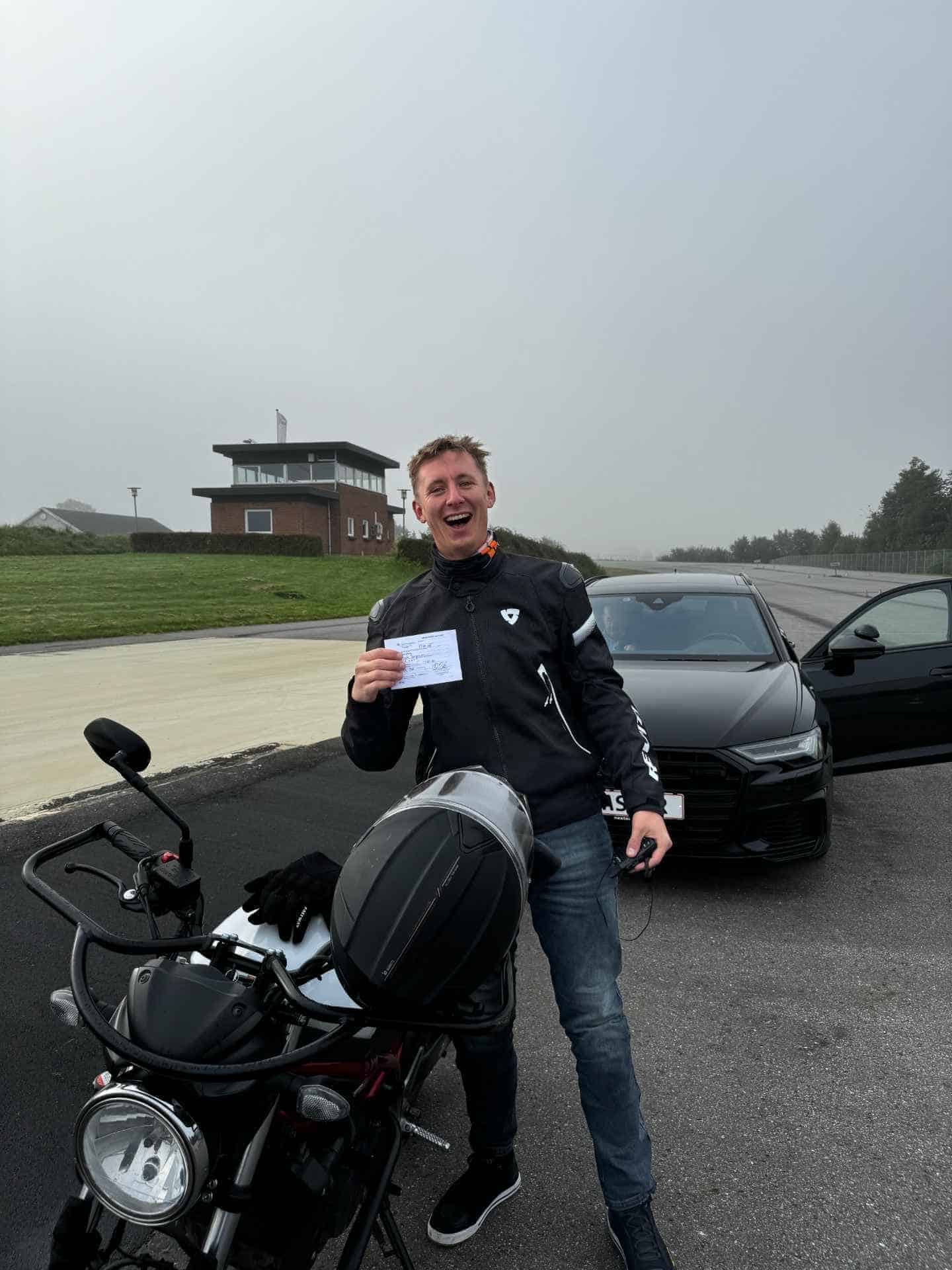 Mand der stolt viser sit beståede teoribevis frem ved siden af en MC